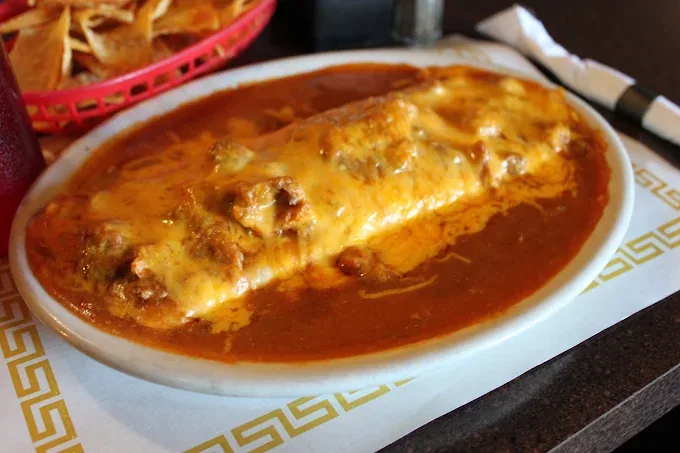 Smothered burrito under red chile sauce and melted cheese, served beside a basket of tortilla chips