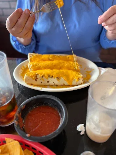 A guest lifting a forkful of smothered burrito, cheese stretching up from the plate