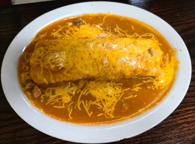 Burrito smothered in red chile sauce and shredded melted cheese on a white plate