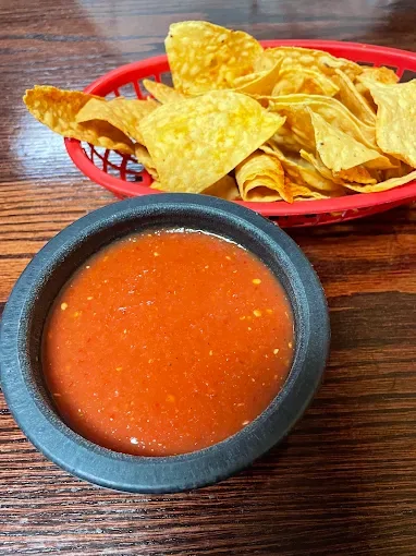A red basket of tortilla chips beside a stone bowl of house salsa
