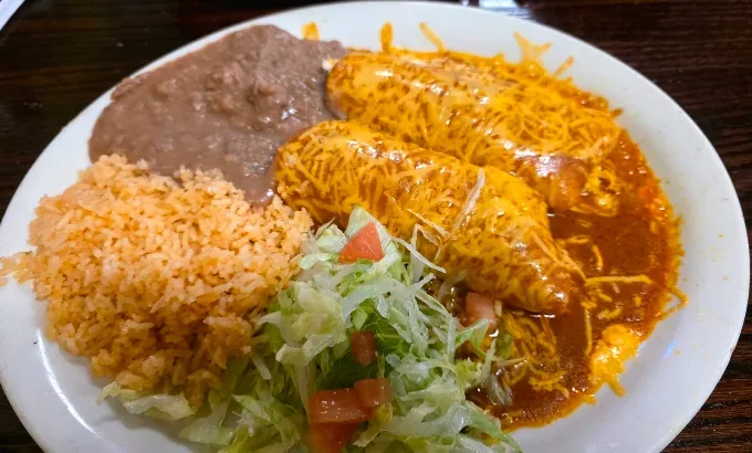 Two enchiladas smothered in red chile and melted cheese, with Mexican rice, refried beans and a lettuce and tomato salad