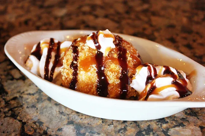 Fried ice cream in a white dish, drizzled with caramel and chocolate and topped with whipped cream