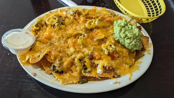 Plate of nachos layered with melted cheese, jalapeños, tomato and a scoop of guacamole